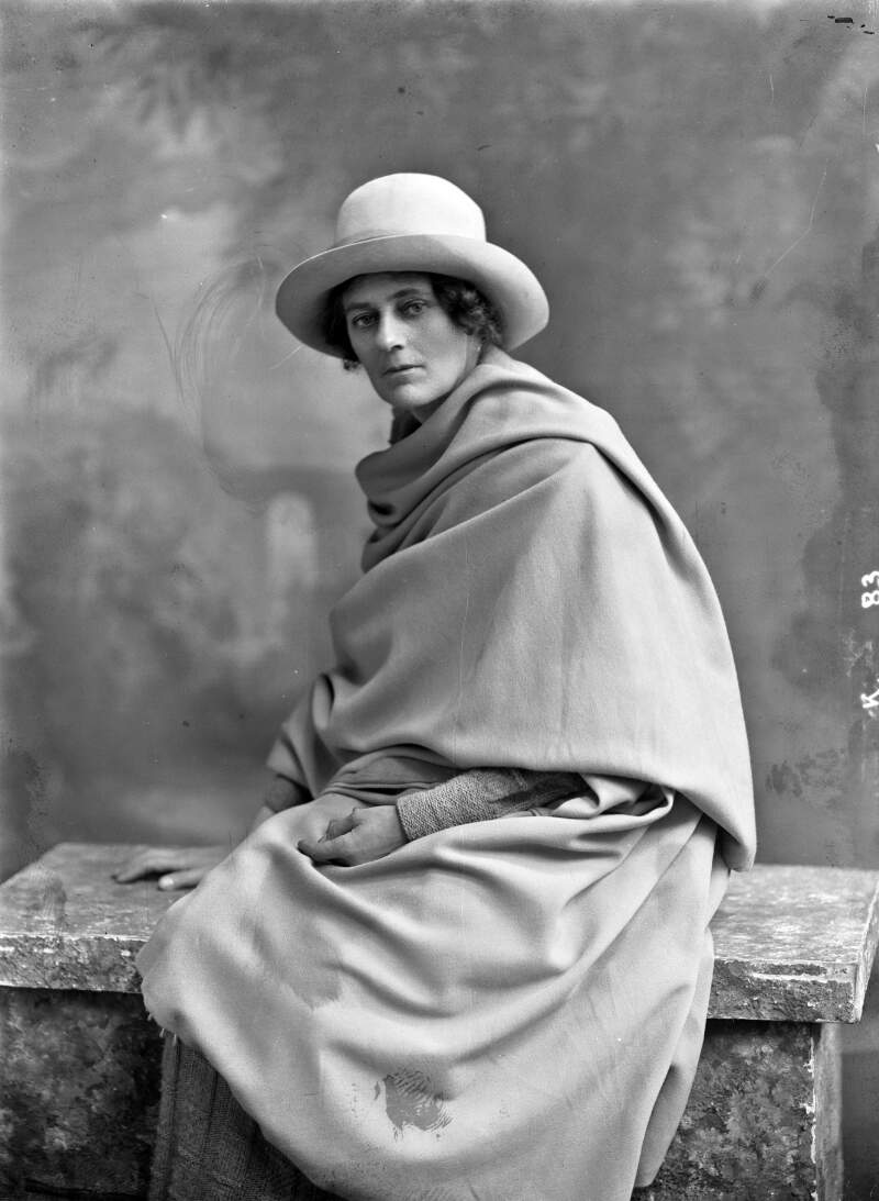 Countess Constance Markievicz wearing cloak and hat, seated, studio three-quarter length portrait]