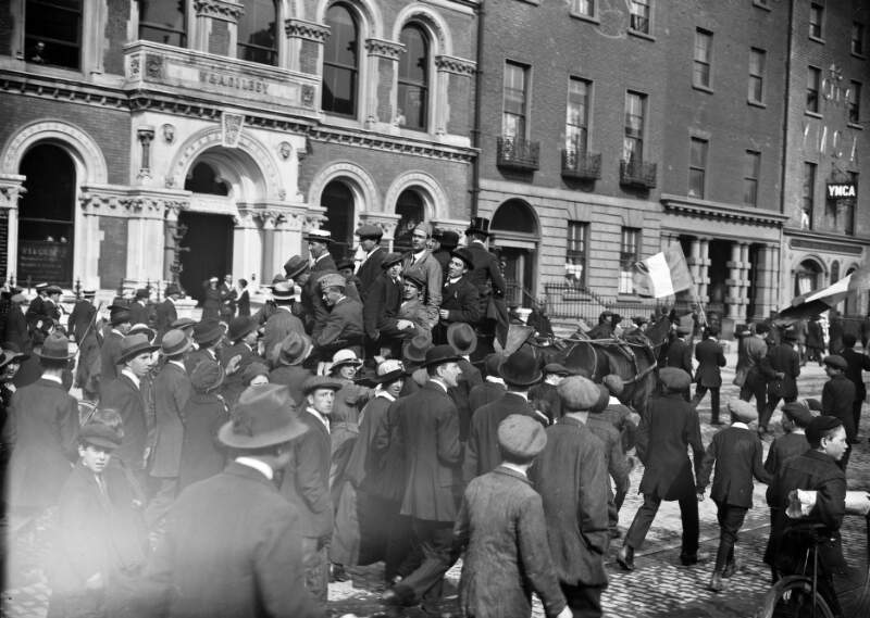 [Released prisoners being brought by horse and cart along Dawson Street through the crowds, passing W.A. Gileey and YMCA buildings]