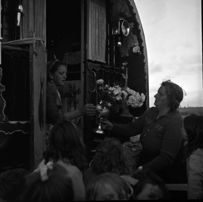 [Woman receiving flowers at caravan door with children onlooking, Buttevant, Co. Cork]