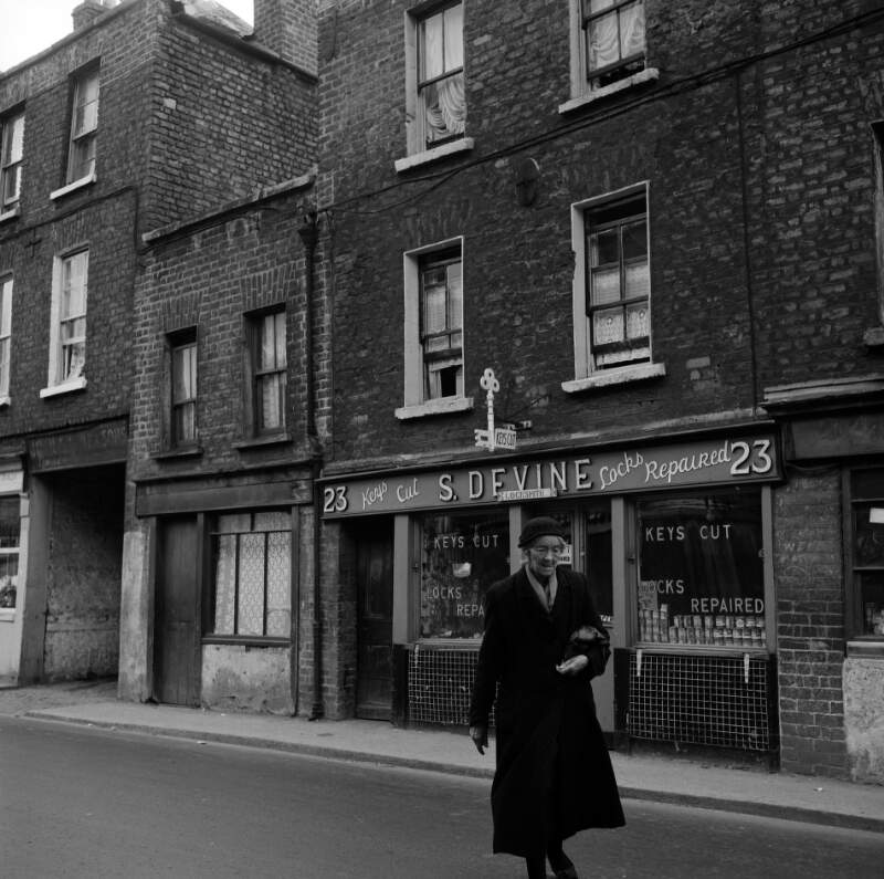 [Woman passing locksmith shop, S. Devine, No. 23, Kevin Street, Dublin]
