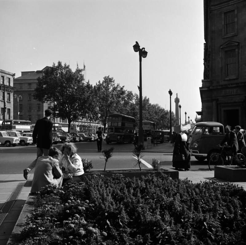 [Two people seated by flower bed, looking onto O'Connell Street, Dublin]