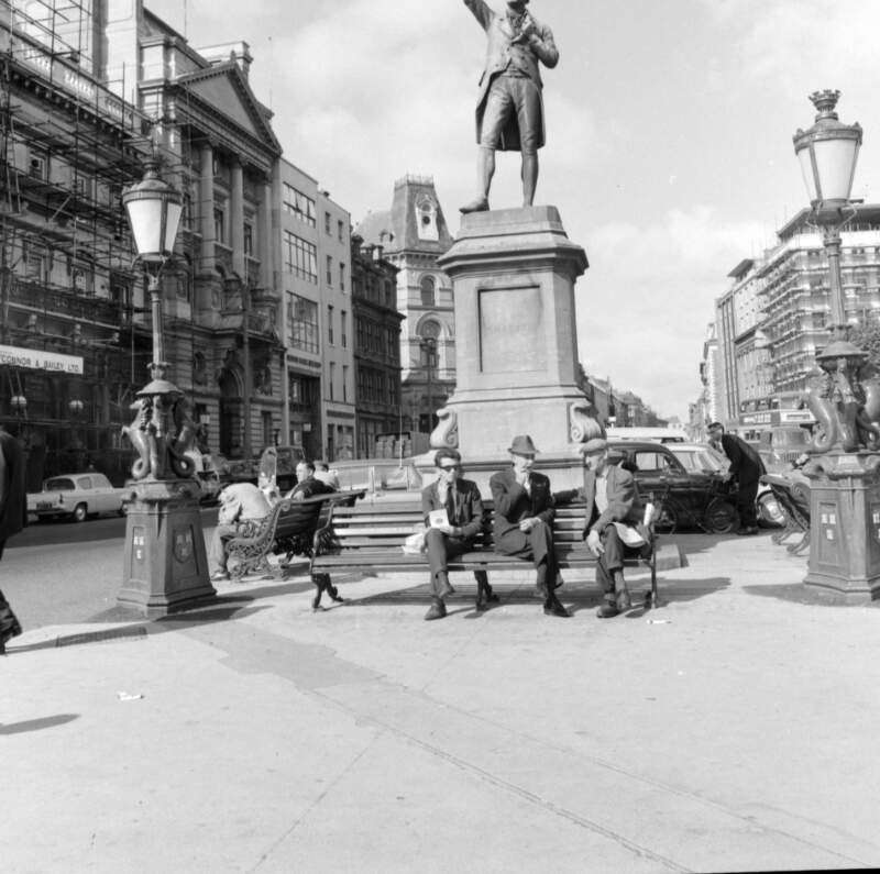 [Group seated near statue of Grattan and ornate lamp posts, Dame Street, Dublin]