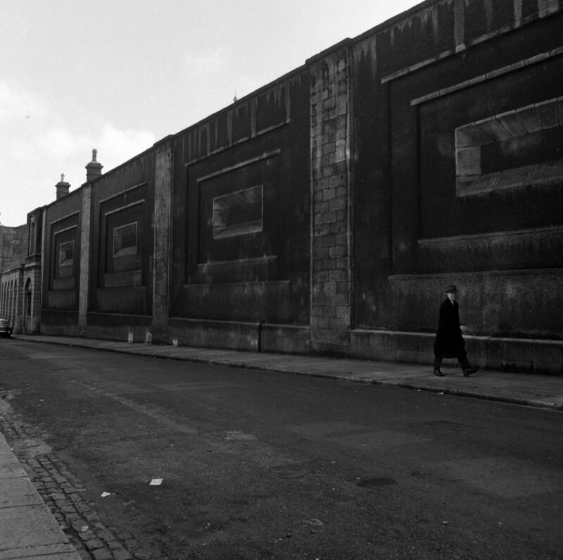 [Man walking alongside wall with rectangular motif, near Dublin Castle]