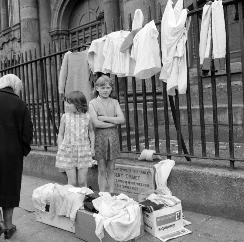 [Elizabeth (Lily) Collins and her friend Angela Arnold, selling secondhand clothes in aid of the charity Gorta as an old woman passes by outside St. Catherine's Church, Thomas Street, Dublin]