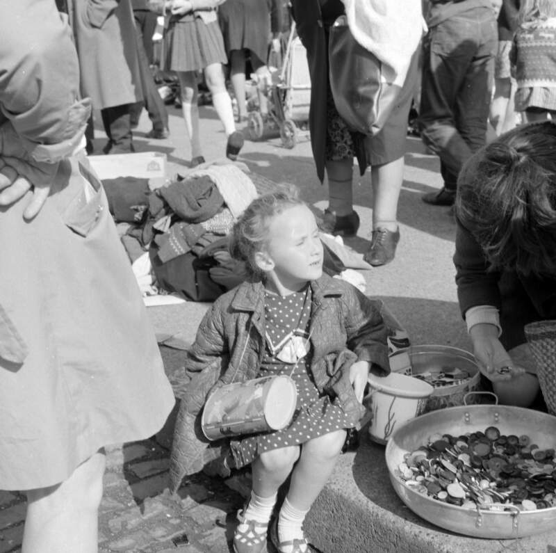 [Little girl, with handbag, sitting beside large bowl of buttons, Cumberland Street Market, Dublin]