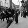 [Patrick Kavanagh pointing from carriage towards man on street, Anthony Cronin seated alongside him, jarvey and group of men gathered outside Davy Byrnes, Bloomsday, Duke Street, Dublin]