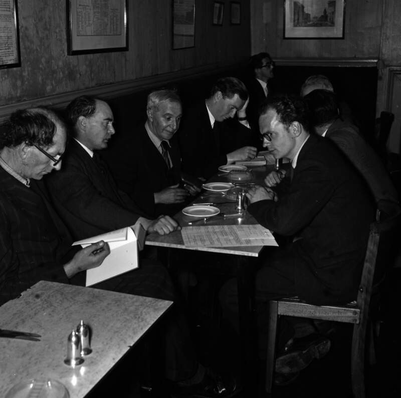[Patrick Kavanagh reading book, Flann O'Brien, Con Leventhal, John Ryan, unidentified man in background, Anthony Cronin at Davy Byrnes pub, Bloomsday, Duke Street, Dublin]