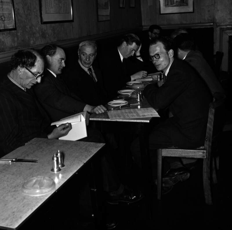[Patrick Kavanagh reading book, Flann O'Brien, Con Leventhal, John Ryan with head in hands, unidentified man in background, Anthony Cronin at Davy Byrnes pub, Bloomsday, Duke Street, Dublin]