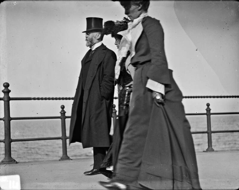 [Left profiles of two women and one man walking along Bray seafront]