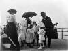 [Group of children standing on Bray promenade with two women and one man]