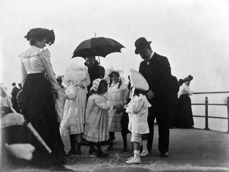 [Group of children standing on Bray promenade with two women and one man]