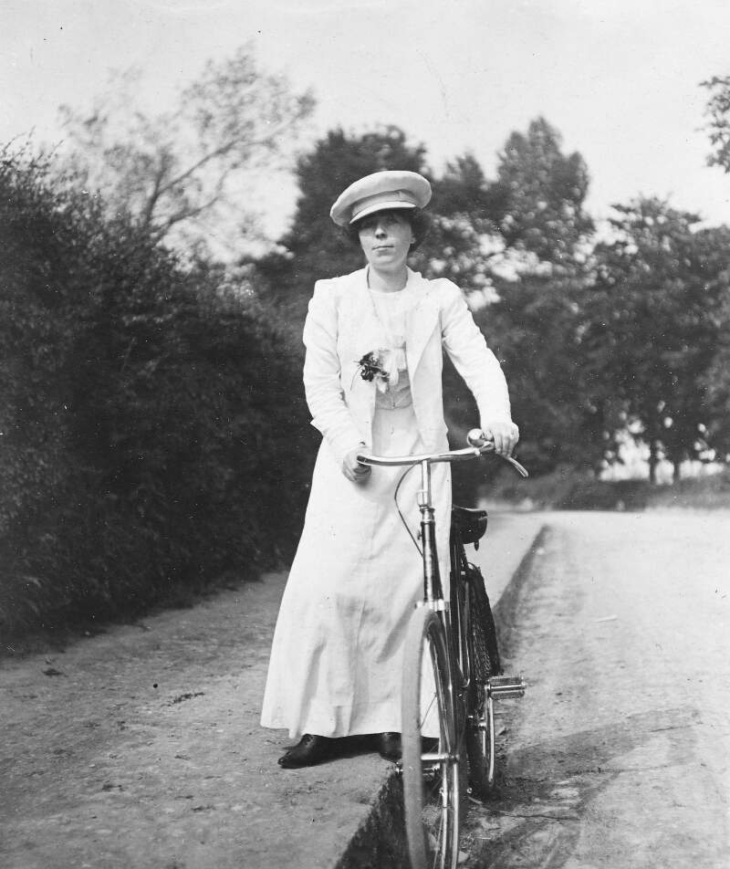 [Woman wheeling bicycle at roadside]