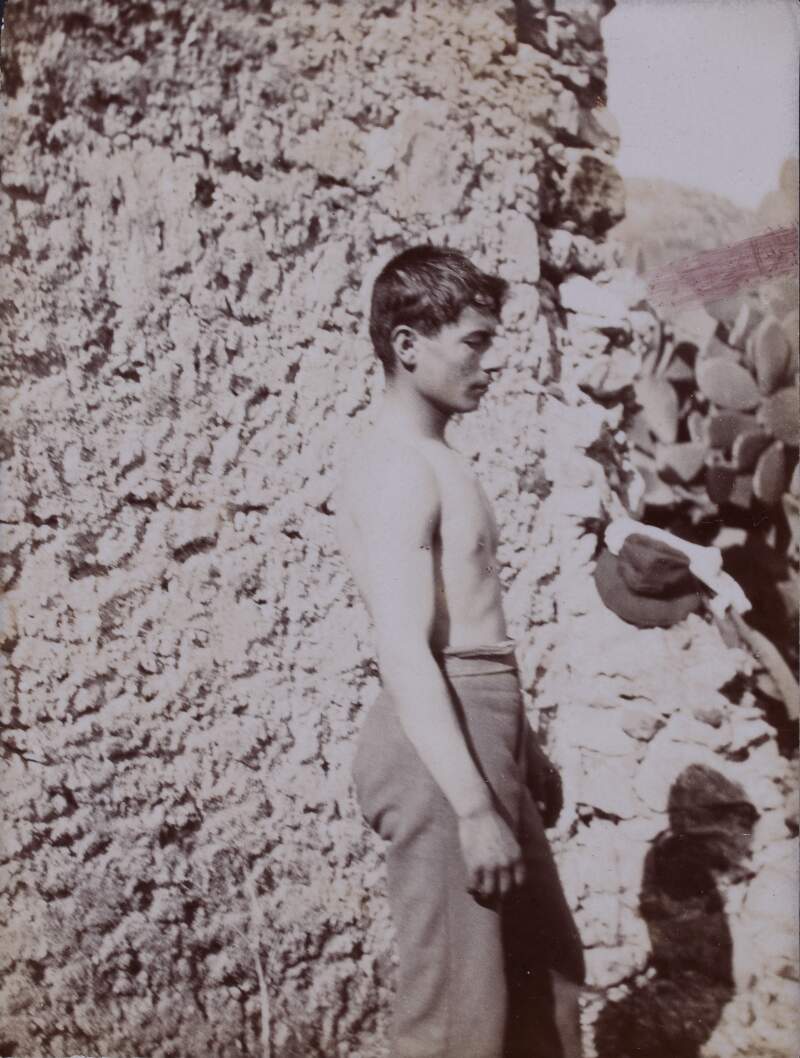 [Sideways profile of a barechested man in front of stone wall]