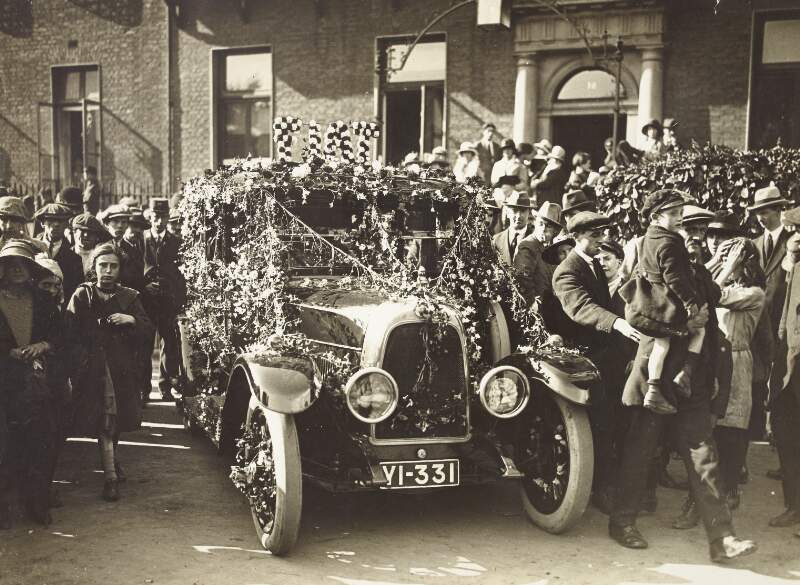 [Fiat car adorned with flowers and surrounded by people at 18 Rutland Square (now Parnell Square), Dublin]