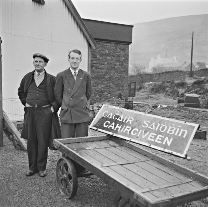 Booking clerk P. J. Scott and other standing next to sign for Cahirciveen, Cahirciveen, Co. Kerry.