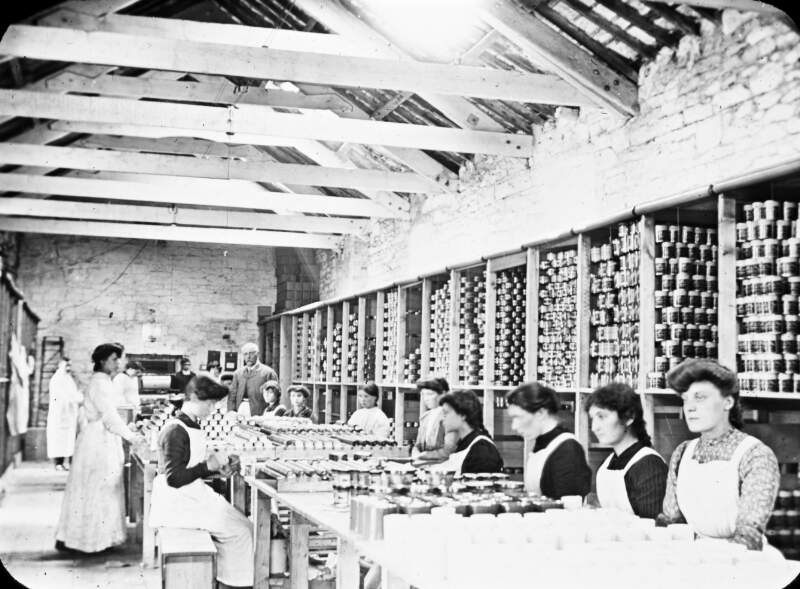 Shaw & Sons. Painting & labelling department, tins and glass jars. All young women and girls, with foreman. Stacks of tins.