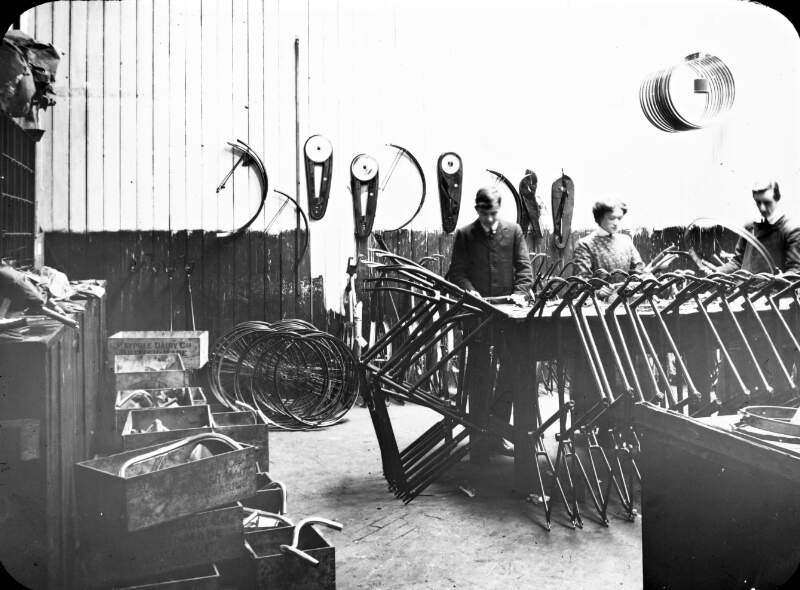 O'Neills. Bicycle inspection room: all parts, pre-assembly. One woman and two men.