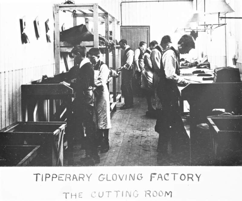 Tipperary Gloving Factory. No 98 The Cutting Room. Young boys and young men at bench, with leather pieces.