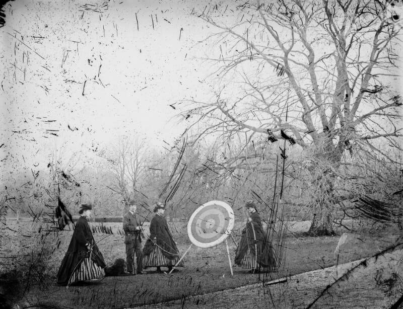 [One woman and three men on lawn, playing archery. Women with crinolines hitched up to reveal stripped petticoats.]