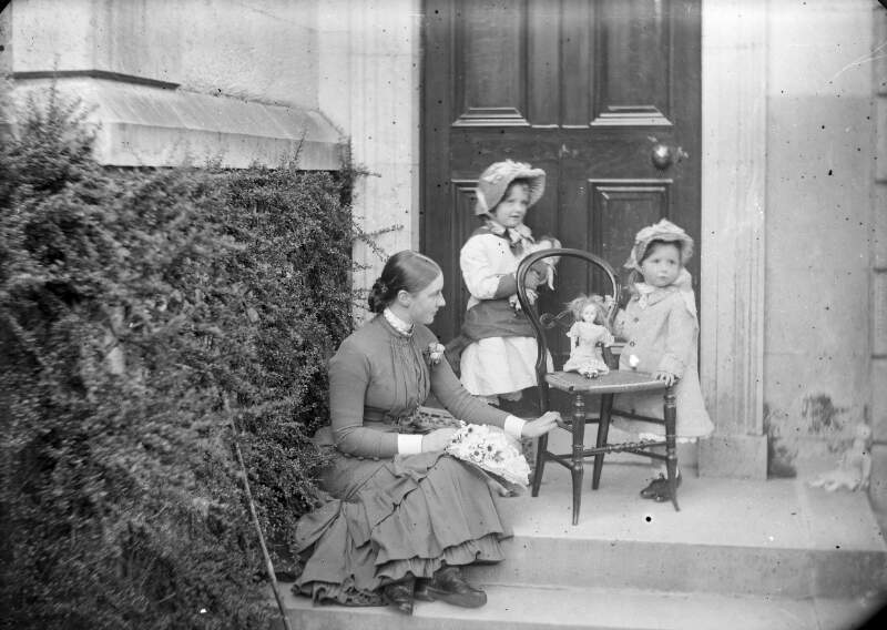 [Ethel and Edith Dillon playing with dolls on steps of house. Both wearing bonnets and coats, accompanied by older sister Georgiana]