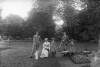 [Family group on Clonbrock lawn, two young men and a woman seated, gardening implements on grass. Includes Robert Dillon, Georgiana Dillon (seated) and young Edith and Ethel.]