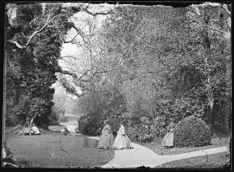 [28/04/64. Women in crinolines walking in grounds.]