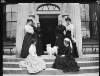 [Group of women on steps of Clonbrock House looking at small dog. Includes Augusta Dillon (centre left). Portico and doorway in background.]