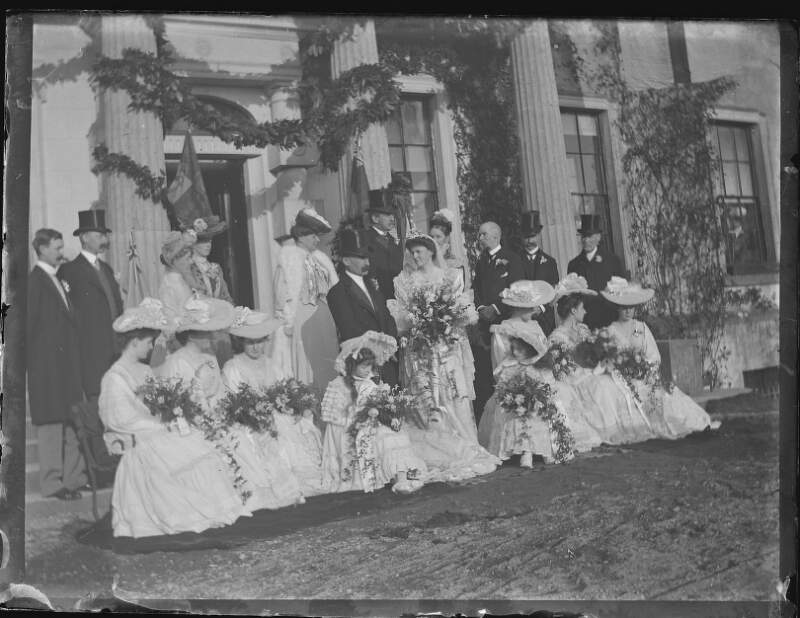 [Wedding party in front of Clonbrock House which is decorated with garlands. Lord and Lady Clonbrock at centre/back - 4th Lord Clonbrock, Gerald Dillon and Augusta Crofton Dillon. All women carrying large bouquets, men wearing top hats - Edith Dillon's marriage to Sir William Mahon.]