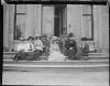 [Group (Five women, two men and a child) seated on steps of large house. Women wearing wide brimmed hats. Includes Lord Clonbrock and Augusta Dillon.]