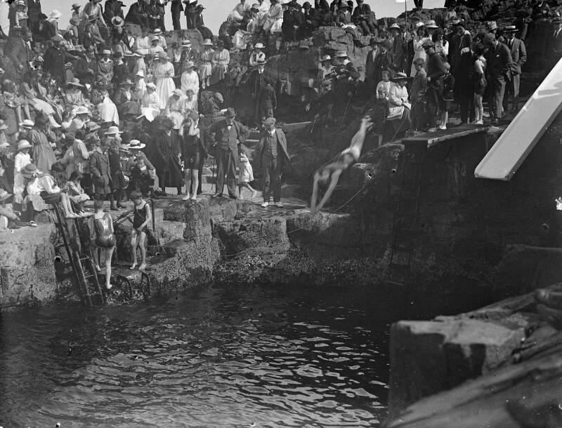 [Diving competition. Crowd gathered around to watch young man diving into harbour.]