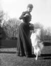 [Bobs walking and A.F.K.T. Dog standing on his hind legs beside elderly woman holding box camera. Trees and parkland in the background. Location Clonbrock.]
