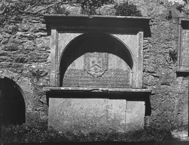 [Kilconnell 1901. Tomb with inscription dating from 1680s. Crest of arms incorporating three flowers over the inscription.]
