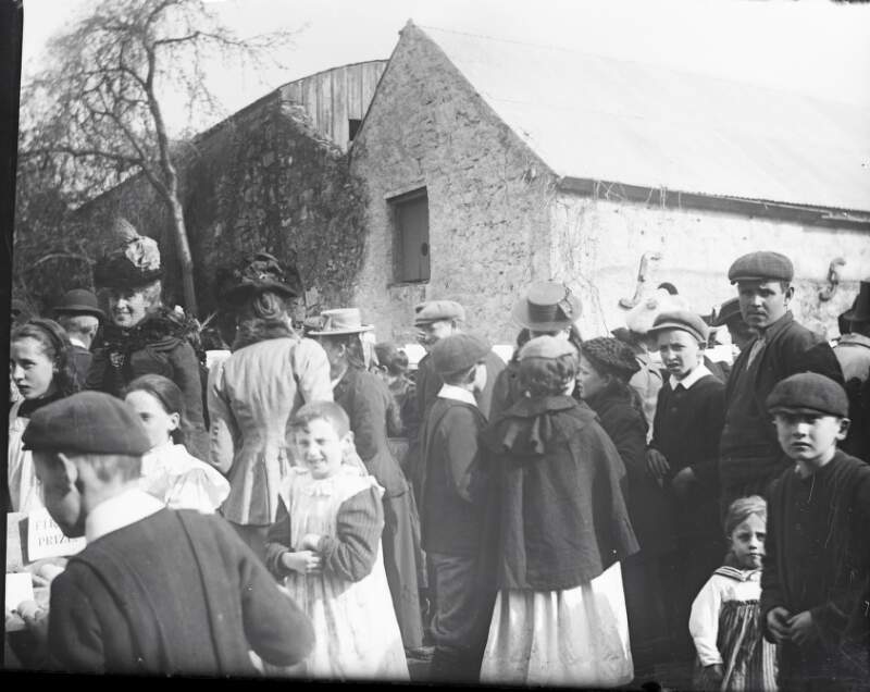 [Home, poultry show, looking up garden 1902. Men, women and children gathered in yard. Young girls wear pinafores, boys and men wear caps. Outhouse in background.]