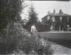 [Eardisland House, reversed 1902. View of woman standing by tall flower beds, two storey ivy covered house in background.]
