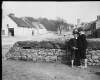 [Ahascragh, looking towards chapel. Two young boys (barefoot) standing beside stone wall on main street of Ahascragh. Shop "Hurley" on main street.]