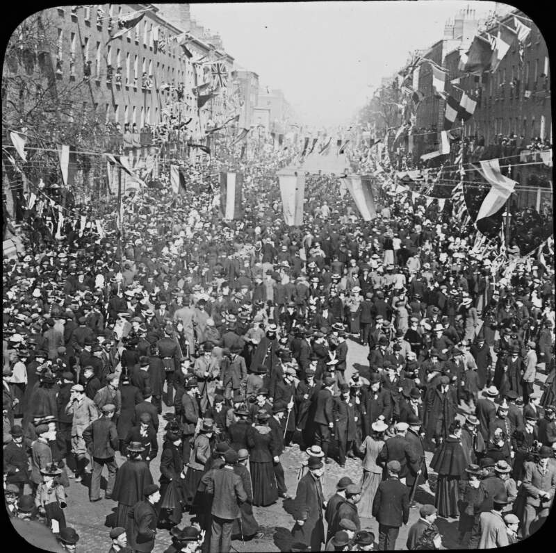 [Crowd at Fitzwilliams place. Large crowd on street decorated with banners and flags. T.Mason, 5 Dame Street, Dublin. Possibly on occasion of Royal visit, 1900.]