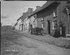 [Ahascragh. Village of Ahascragh showing donkey and cart, two women and boy standing outside house. Street is partially cobbled.]