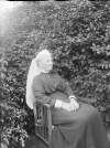 [Augusta Crofton Dillon seated outdoors, Large bush/shrub in background, Augusta wears a long scarf style head dress, similar image to Clonbrock 1168.]