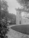 [Chapel 1926 Exterior. Church with spire leaf strewn, pathway in foreground. Headstones also visible St. Catherine's Church was damaged in1922 and was then repaired and reopened in 1926.]