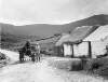 [Connemara 1903. Pony and trap stopped outside thatched stone cottage. Mountainous in background, bare foot child near man wearing tweeds.]