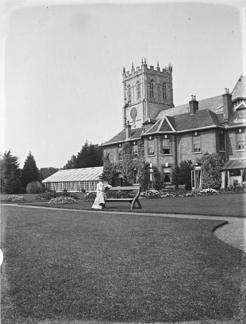 [Boxhill/Christ Church. Woman seated on garden bench in front of large house with tower.]