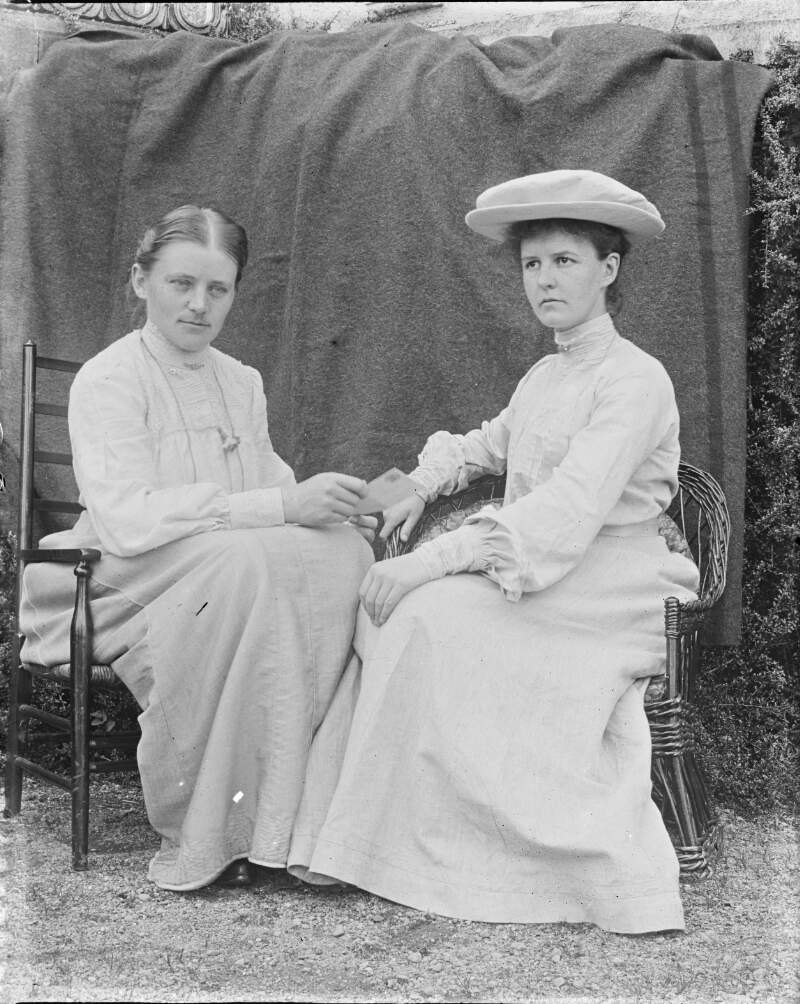[Two women sitting on chairs one of the women is holding a small booklet out to the other. Edith Dillon on left.]