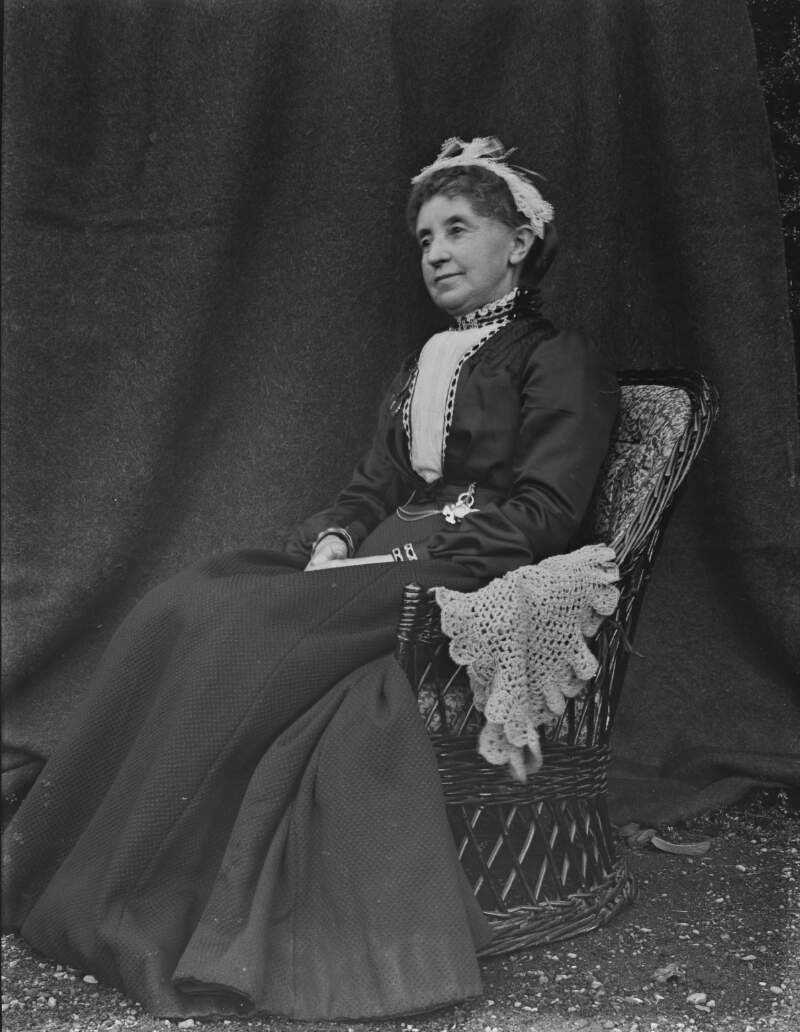 [Woman seated on cane chair.]