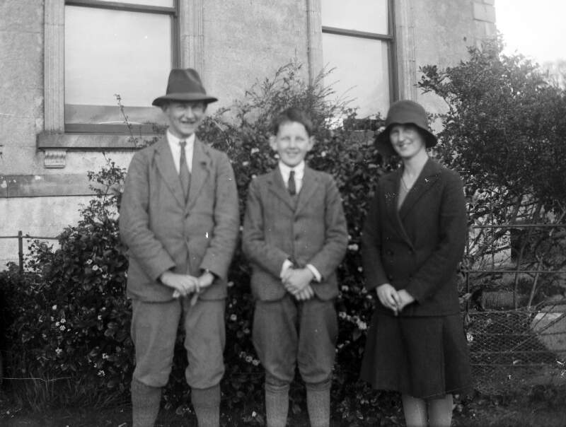 [Man, woman and young boy, with a house in the background.]