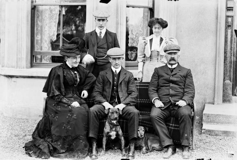 [Group portrait of two men, two women and two dogs in front of window.]