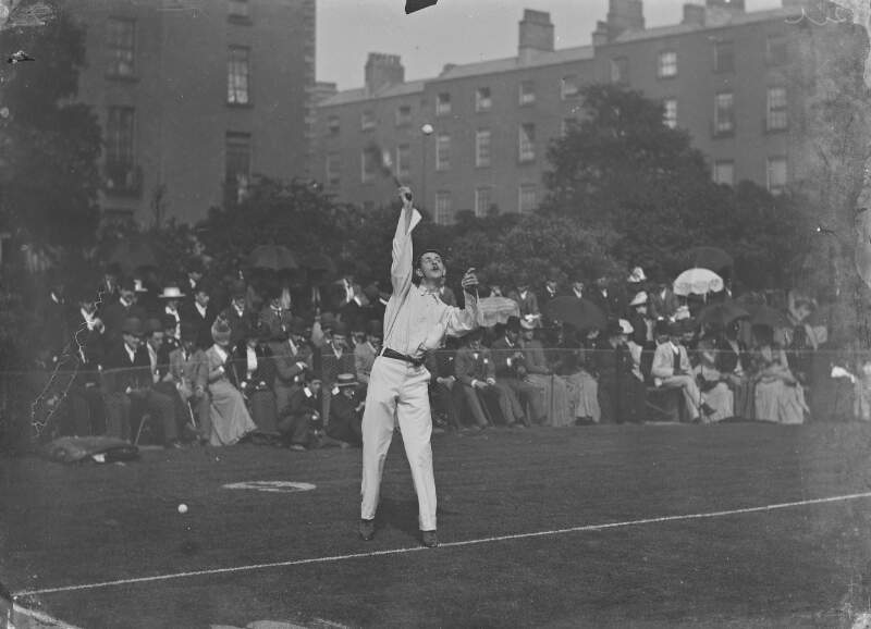 [Spectators at tennis courts watching a man about to serve (possibly at Fitzwilliam Square).]