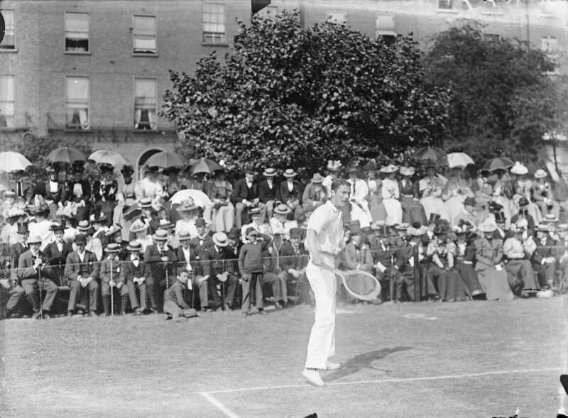 [Spectators at tennis courts watching a man play (possibly at Fitzwilliam Square).]