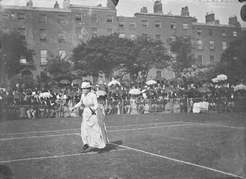[Tennis. Spectators watching a woman with a long dress with bustle playing tennis. Possibly at Fitzwilliam Square.]