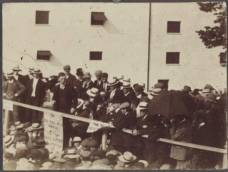 [Speaker addressing a political rally from a crowded platform],