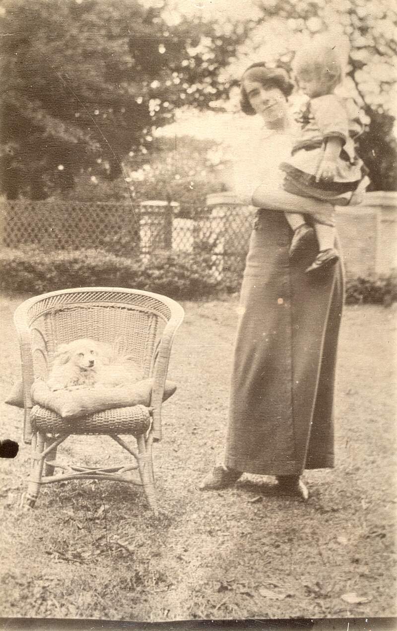 [Muriel Gifford MacDonagh holding Donagh MacDonagh in her arms, with their dog Flip seated in chair beside them]